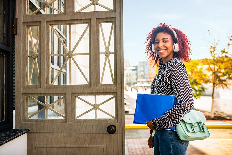 A young woman with curly red hair walking into the post office with a large envelope