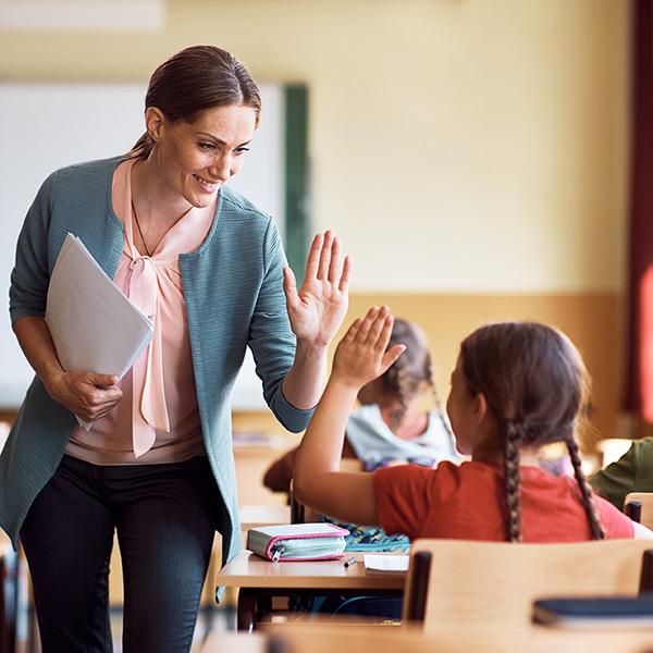 Happy teacher and schoolgirl giving high five during class at school